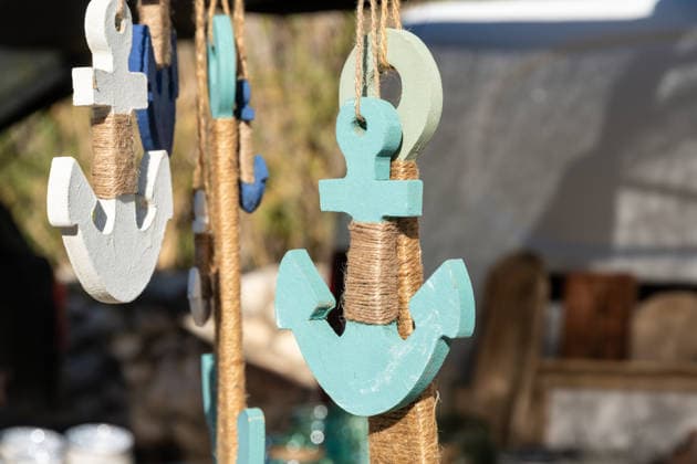Hängende hölzerne Ankerdekoration mit Juteseil umwickelt Handcrafted wooden anchor decorations in blue, white, and turquoise, wrapped with jute rope, hanging from strings at an outdoor market stall (License=RF) Copyright: xZoonar.com DetlefxVoigtxinfo@gph-foto.dex 24337947