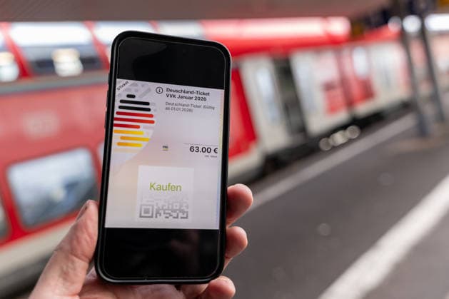 Deutschlandticket mit neuem Preis am Bahnhof 17.12.25, Limburg: Symbolfoto, Illustrationsbild, Symbolbild, Illustrationsfoto, Alltagsszene Ein Smartphone zeigt das digitale Deutschlandticket mit einem Preis von 63 Euro. Das Mobiltelefon wird auf einem Bahnsteig gehalten, im Hintergrund ist ein roter Zug unscharf zu sehen. Das Bild steht im Zusammenhang mit der geplanten Preiserhöhung des Deutschlandtickets zum 1. Januar 2026 sowie mit dem öffentlichen Nahverkehr und dem Bahnverkehr in Deutschland. Limburg Hessen Copyright: xThorstenxWagnerx