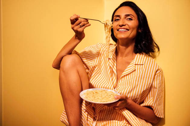 Frau, die einen Teller Spaghetti genießt, während sie in einer gemütlichen Ecke sitzt, in einem gestreiften Pyjama, mit einem fröhlichen Gesichtsausdruck, der ein entspanntes Esserlebnis zu Hause zeigt Female enjoying spaghetti in cozy corner, wearing striped pajamas, smiling while holding fork, creating a warm and inviting atmosphere for home dining (License=RF) ,model released, Symbolfoto Copyright: xZoonar.com DashaxPetrenkox 24395936 ,model released, Symbolfoto ,property released