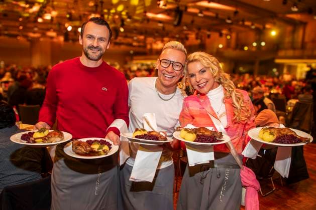 abb: David Biethig, Sascha Lauterbach und Victoria Herrmann als Promi Kellner beim Servieren von Teller mit Gaensekeuele Rotkohl und Kloesse bei der 31. Frank Zander Weihnachtsfeier Weihnachtsessen fuer Obdachlose und Beduerftige Menschen 2025 im Estrel Convention Center am 22.12.2025 in Berlin Berlin Deutschland