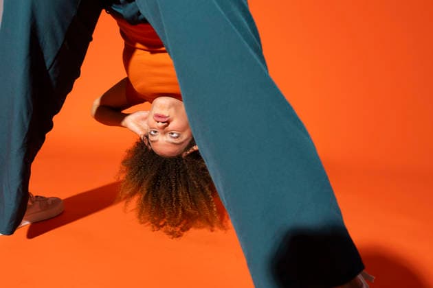 Playful young woman looking through legs in front of orange background model released, Symbolfoto, MIKF00533