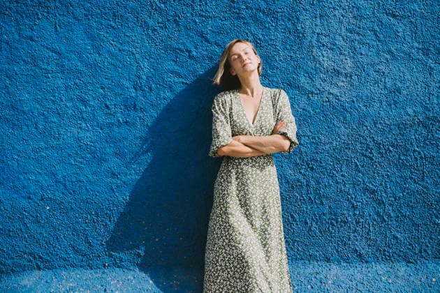 Relaxed woman in green dress leaning against blue wall in sunlight model released, Symbolfoto, NDEF03055
