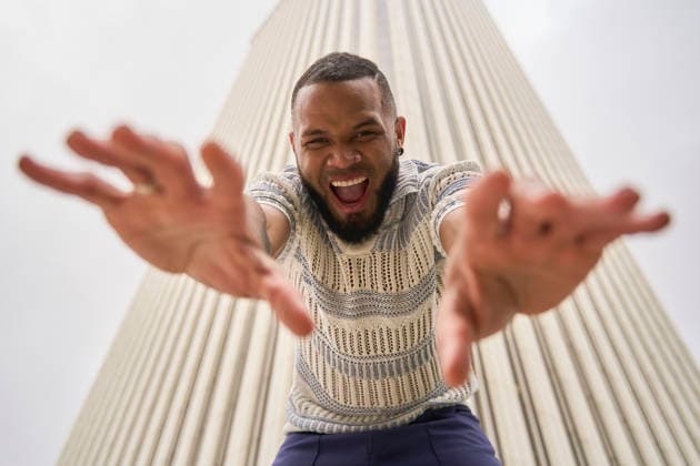 Joyful playful person reaching out energetically in front of tall building model released, Symbolfoto, OMSF00086