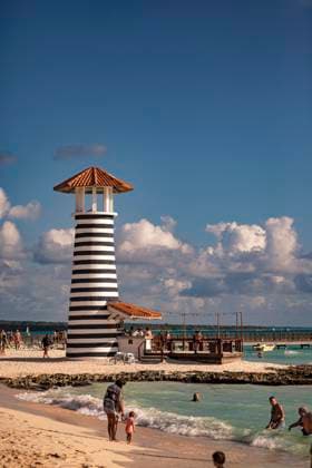 Tourists enjoying dominican republic beach with iconic striped lighthouse Bayahibe, Dominican Republic 1 January 2025: Tourists relaxing on the beach near a black and white striped lighthouse in dominicus, dominican republic, a popular caribbean destination, 64091164.jpg RECORD DATE NOT STATED