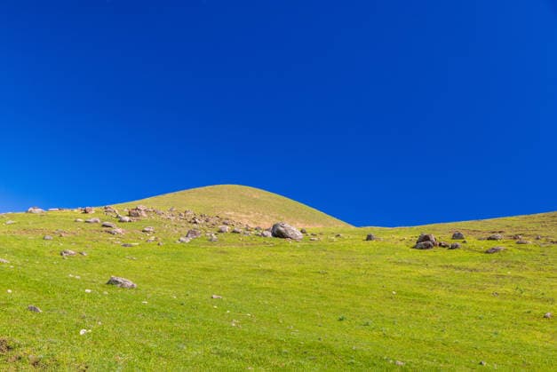 Creative Highlights World Green grassy hill with scattered rocks under a deep blue cloudless sky Green grassy hill with scattered rocks under a deep blue cloudless sky, captured in spring daylight in rural Kyrgyzstan, 97039330.jpg RECORD DATE NOT STATED