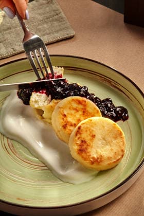 IMAGO Creative, Food, High Protein Frühstück Woman eating syrniki with blueberry jam and sour cream using fork and knife Close-up of delicious syrniki served with blueberry jam and sour cream, being enjoyed by a woman, 97421098.jpg RECORD DATE NOT STATED