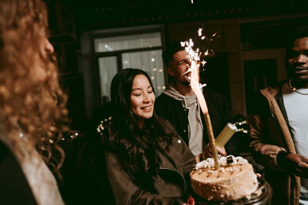 Friends celebrate with cake and sparklers at a birthday party during the evening gathering A group of friends gathers in a cozy setting to celebrate a birthday. One person holds a cake adorned with candles while others enjoy the festive atmosphere, sparkling lights around them., model released, , 97479872.jpg RECORD DATE NOT STATED