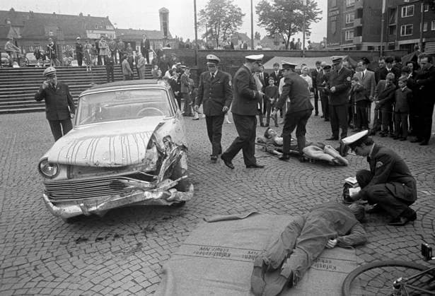 Sechzigerjahre, 31.08.1969, Rettungseinsatz in Bottrop nach einem Verkehrsunfall zwischen Pkw und Fahrrad, Sanitaeter leisten den Verletzten Erste Hilfe, Passanten schauen zu, Deutschland, Bottrop, Ruhrgebiet, Nordrhein-Westfalen, NRW Sechzigerjahre, 31.08.1969, Verkehrswesen, Strassenverkehr, Darstellung Rettungseinsatz auf dem Berliner Platz in Bottrop nach einem Verkehrsunfall zwischen einem Pkw und einem Fahrradfahrer, Uebung und Training, Sanitaeter leisten Erste Hilfe am verletzten Radfahrer und dem Autofahrer, Maenner, Frauen und Kinder beobachten die Aktion, Deutschland, Bottrop, Ruhrgebiet, Nordrhein-Westfalen, NRW, Sixties, 31.08.1969, road traffic, illustration of a rescue mission on the Berlin Square in Bottrop after a street ac