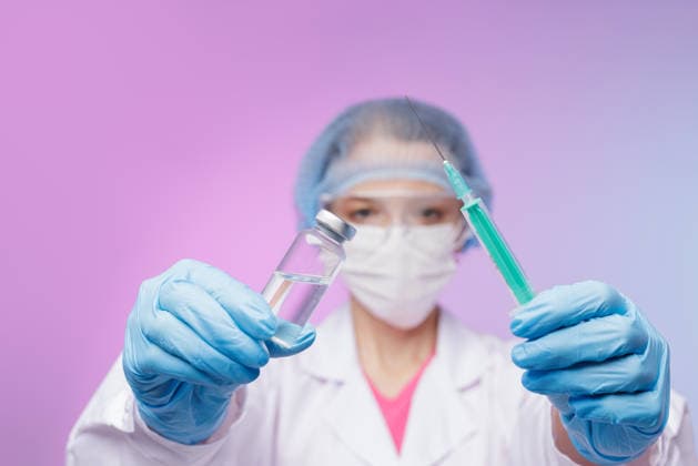 Female medical professional wearing PPE holds syringe and vaccine vial towards camera, emphasizing immunization, safety, and healthcare responsibility during global pandemic. Doctor in protective uniform presents syringe and vaccine vial, symbolizing trust, medical care, immunization, and modern healthcare procedures., model released, , 97739450.jpg RECORD DATE NOT STATED
