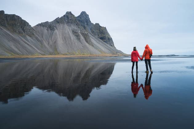 Couple Taking in Vestrahorn on Reflective Black Sand Beach Vik, Mýrdalshreppur, Iceland CR_GASU260104-1929930-01 ,model released, Symbolfoto
