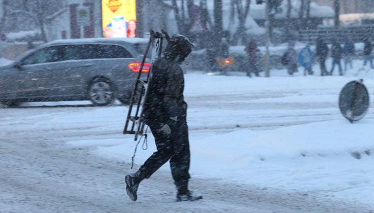 Schneetreiben am Donnerstagmorgen in Hamburg. Ein Mann geht mit einem Schlitten auf der Schulter über eine mit Schnee bedeckte Straße. Barmbek Hamburg