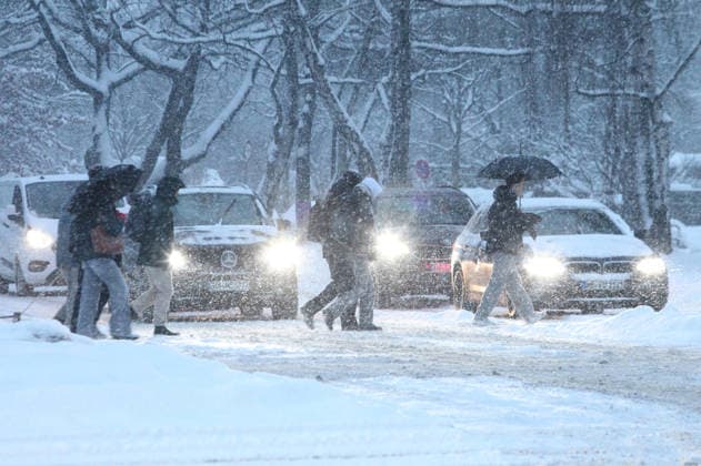 Schneetreiben am Donnerstagmorgen in Hamburg. Passanten gehen mit Regenschirmen über eine mit Schnee bedeckte Straße. Winterhude Hamburg
