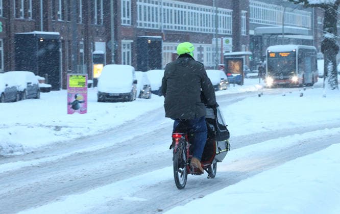 Schneetreiben am Donnerstagmorgen in Hamburg. Ein Mann fährt mit seinem Lastenrad auf einer mit Schnee bedeckten Straße. Barmbek Hamburg