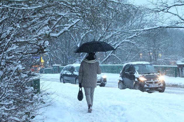 Schneetreiben am Donnerstagmorgen in Hamburg. Ein Mann geht mit einem Regenschirm auf einem mit Schnee bedeckten Gehweg entlang. Barmbek Hamburg