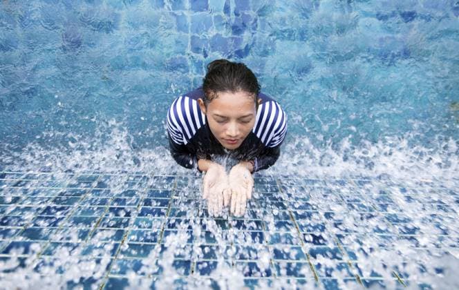 Junge Frau in einem Ganzkörper Badeanzug nimmt Wasser, um die Handflächen im blauen Pool zu öffnen Young woman in a full-body swimsuit taking water to open palms in the blue pool Copyright: imageBROKER MilanxVasicek ibxiqx15874695.jpg ,model released, Symbolfoto ,property released