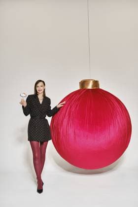 Frau steht neben einem großen roten Ornament in einem Studio. Sie hält ein kleines Objekt in der rechten Hand und hat einen verspielten Gesichtsausdruck. Der Hintergrund ist schlicht und unterstreicht das festliche Thema Woman stands next to a large red ornament in a studio. She holds a small object in her right hand and has a playful expression. The background is plain and highlights the festive theme Copyright: imageBROKER AlekseixIsachenko ibxaii16264854.jpg ,model released, Symbolfoto ,property released