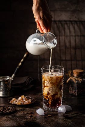 Eiskaffee in einem hohen Glas Ice coffee in a tall glass with cream poured over, sugar and coffee beans on dark background (License=RF) Copyright: xZoonar.com TatianaxGoskovax 24482045