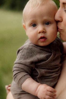 Mother holding and kissing baby in floral dress outdoors Amsterdam, North Holland, Netherlands CR_RTBZ26012089-1947930-01 ,model released, Symbolfoto