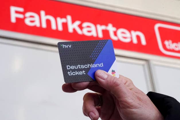 cntv: Deutschlandtiket in der Hand vor HVV Bus und Bahnen Deutscxhe Bahn Deutschlandticket ist ein monatliches Abonnement für den gesamten deutschen ÖPNV OEPNV oeffentlichen Nahverkehr Busse, Straßenbahnen, U-Bahnen, S-Bahnen, REs, RB). Es kostet seit Januar 2026 63,00 Euro pro Monat und Fahrgast und gilt deutschlandweit Hamburg Germany