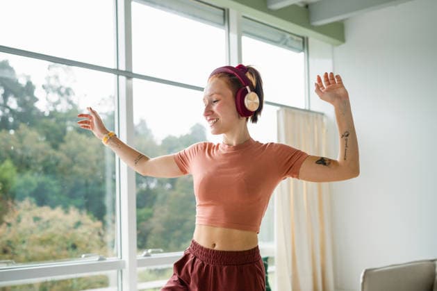 Happy woman dancing indoors with headphones by window in casual clothes model released, Symbolfoto property released, ATSF00154