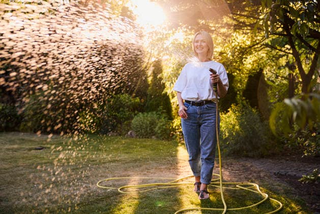 Smiling woman watering lawn with hose outdoors at sunset in summer model released, Symbolfoto property released, BSZF02960