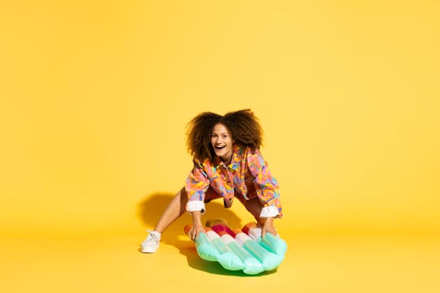 Woman with curly hair holding ice cream shaped pool raft against yellow background model released, Symbolfoto, MIKF00572