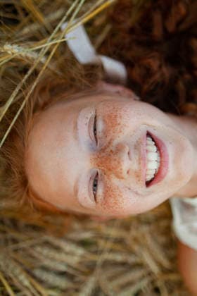 Smiling with red hair and freckles lying in wheat field wearing white dress model released, Symbolfoto, VCF01121