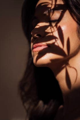 Eine Frau mit langen dunklen Haaren, die von sanftem Licht beleuchtet wird, hat Schatten von nahegelegenen Pflanzen auf ihrem Gesicht, was eine ruhige und künstlerische Atmosphäre in einer minimalistischen Umgebung schafft. Female figure with dark hair, bathed in soft light, has delicate shadows from plants on her face, enhancing the tranquil and artistic ambiance of the scene (License=RF) ,model released, Symbolfoto Copyright: xZoonar.com DashaxPetrenkox 24543695 ,model released, Symbolfoto ,property released