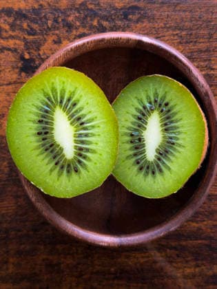 Kiwi-Frucht-Hälften in Holzschale, Draufsicht Top view of fresh green kiwi sliced in half inside a rustic wooden bowl, showing vibrant texture, seeds, and healthy tropical fruit concept. (License=RF) Copyright: xZoonar.com KellyxDengesx 24550538