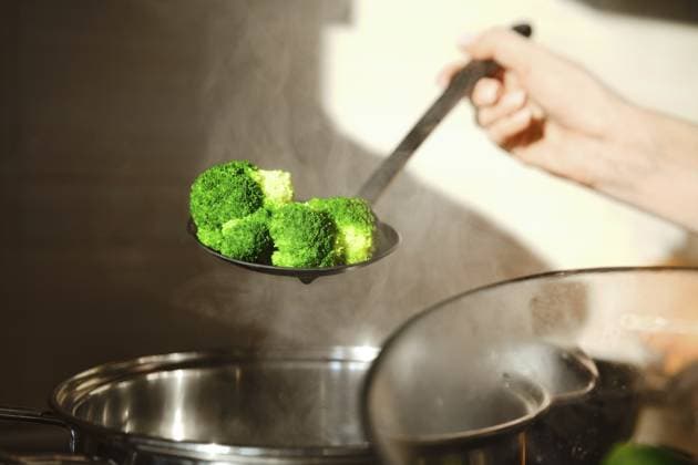 Eine Person hält einen Schaumlöffel mit gedämpftem Brokkoli über einen Topf in einer Küche. Der Dampf steigt auf und zeigt die Hitze, die beim Kochen entsteht A person holds a slotted spoon with steamed broccoli above a pot in a kitchen. The steam rises, showing the heat from cooking Copyright: imageBROKER AlekseixIsachenko ibxaii16456926.jpg ,model released, Symbolfoto ,property released
