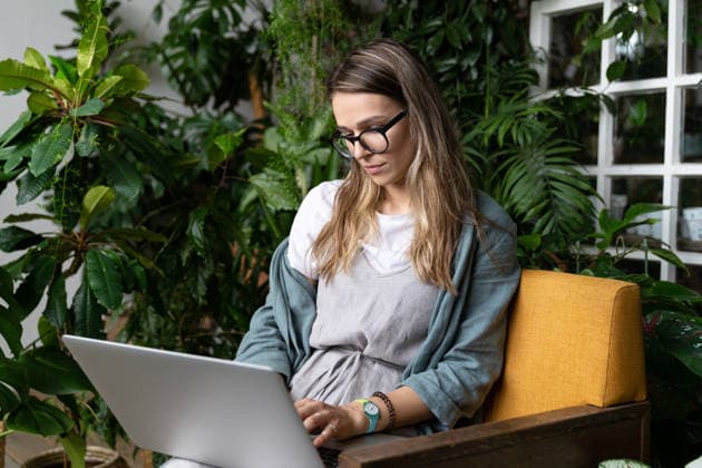 Gärtnerin sitzt auf einem Stuhl im Gewächshaus und arbeitet an ihrem Laptop, umgeben von Pflanzen, Remote-Arbeit, Telearbeit. Woman gardener wear linen dress, sitting on chair in green house, working on laptop surrounded by plants. Home garden, remote work, distance job. (License=RF) ,model released, Symbolfoto Copyright: xZoonar.com DmitriixMarchenkox xEnvatox 24565095 ,model released, Symbolfoto ,property released