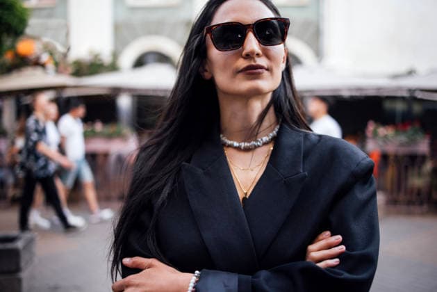 Selbstbewusste Frau mit langen dunklen Haaren, stilvoller Sonnenbrille und schwarzem Blazer steht mit verschränkten Armen in einer lebhaften städtischen Umgebung und präsentiert moderne Mode und Selbstsicherheit. Stylish woman with long dark hair and sunglasses stands confidently in an urban environment, arms crossed, exuding elegance and modern fashion in a lively atmosphere (License=RF) ,model released, Symbolfoto Copyright: xZoonar.com DashaxPetrenkox 24582737 ,model released, Symbolfoto ,property released
