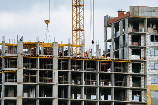 Arbeiter auf der Baustelle, die ein mehrstöckiges Wohn- oder Geschäftshaus errichten und dabei einen Turmdrehkran zum Heben von Materialien verwenden, als Symbol für Stadtentwicklung und zukünftiges Wachstum Unfinished multi-story concrete building with scaffolding and a yellow tower crane lifting materials, showcasing urban construction progress and new infrastructure development (License=RF) Copyright: xZoonar.com ElenaxShishkinax 24089273