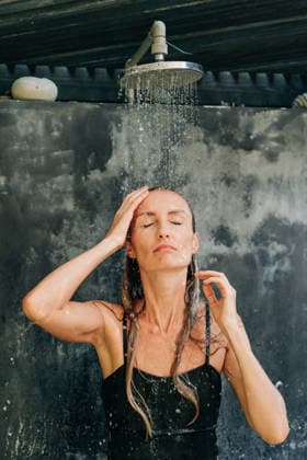Eine Frau in einem schwarzen Badeanzug steht unter einer erfrischenden Dusche im Freien in einem tropischen Resort. A woman in a black swimsuit stands under a refreshing shower outside in a tropical resort. (License=RF) ,model released, Symbolfoto Copyright: xZoonar.com TITOVAxILONAx 24612157 ,model released, Symbolfoto ,property released