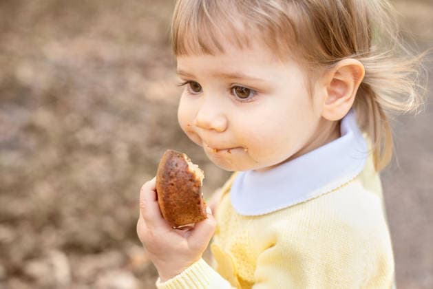 Side view of a toddler enjoying a pastry during a walk outdoors. Wales, England, United Kingdom R_JNDO260208-1946901-01 ,model released, Symbolfoto
