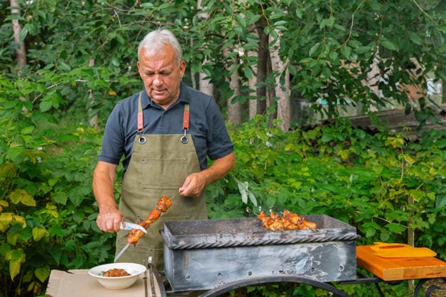 MR_ID32729_23803_AnatoliiIvanovich.jpg, MR_ID32729_23804_NilaAnatoliivna.jpg A man is preparing a barbecue in a lush garden, surrounded by greenery. He is focused on grilling and carving meat skewers, enjoying a relaxed outdoor cooking experience. Model Released Yanishevska_ID32729_1114335_033 Copyright: xYanishevskax