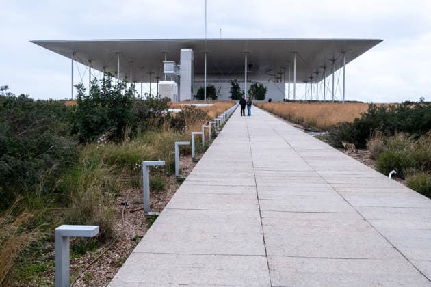 GREECE ATHENS CULTURAL CENTER ROOF PATHWAY ARCHITECTURE Daylight view of visitors walking up the long concrete pathway leading through vegetation to the roof garden of the Stavros Niarchos Foundation Cultural Center in Athens in Attica in Greece on March 13, 2023 The modern building with its large flat roof appears at the end of the path framed by ornamental grasses and low metal lights Daylight view of visitors walking up the long concrete pathway leading through vegetation to the roof garden of the Stavros Niarchos Foundation Cultural Center in Athens in Attica in Greece on March, 2023 Foundation Cultural Center in Athens, Attica, Greece March 13, 2023 The modern building with its broad flat roof stands out at the end of the path framed 