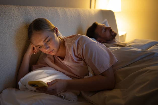 Müde Frau scrollt spät auf ihrem Smartphone und kann sich vor dem Schlafengehen nicht vom Internet trennen, Prokrastination Exhausted woman using smartphone in bed at night struggling with sleep due to social media overuse. Online activity, difficulty falling asleep, compulsive phone checking, web feed social media habit (License=RF) ,model released, Symbolfoto Copyright: xZoonar.com DmitriixMarchenkox 24649724 ,model released, Symbolfoto ,property released