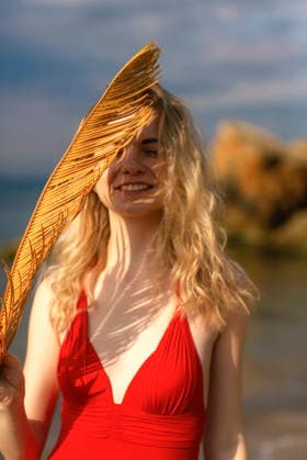 Schöne junge Frau mit blonden Haaren posiert am Strand in einem roten Bikini Beautiful young woman with blond hair posing on the beach in a red bikini. She enjoys the wind, smiles. In her hands is a palm leaf, a figured shadow on her face on a summer day. High quality photo. (License=RF) ,model released, Symbolfoto Copyright: xZoonar.com HannaxNikulnikovax 23896503 ,model released, Symbolfoto ,property released
