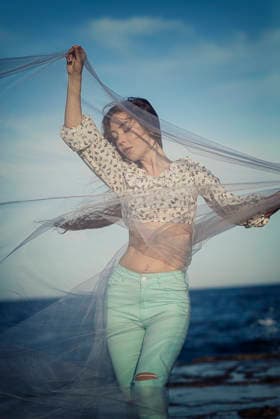 Porträt einer Frau, die ein Chiffontuch in den Händen hält, das im Wind flattert Portrait of a woman holding a chiffon cloth in her hands, which is fluttering in the wind. She is standing on a concrete pier with the sea in the background. Her long hair is fluttering in the wind (License=RF) ,model released, Symbolfoto Copyright: xZoonar.com HannaxNikulnikovax 23941420 ,model released, Symbolfoto ,property released