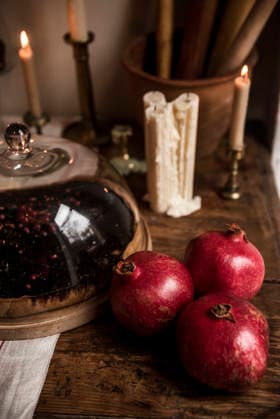 Drei rote Granatäpfel auf einem Holztisch. Three red pomegranates on a wooden table. There are candles in the background. (License=RF) Copyright: xZoonar.com HannaxNikulnikovax 24152781