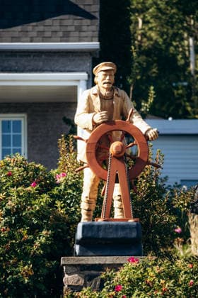 Tadoussac, Kanada ? 22. August 2025: Holzstatue eines Seemanns mit einem Schiffssteuerrad, ausgestellt in einem kleinen Garten im Dorf Tadoussac, umgeben von Blumen und traditionellen Häusern im Hintergrund. Tadoussac, Kanada ? 22. August 2025: Holzstatue eines Seemanns mit einem Schiffssteuerrad, ausgestellt in einem kleinen Garten im Dorf Tadoussac, umgeben von Blumen und traditionellen Häusern im Hintergrund. (License=RM) Copyright: xZoonar.com AndreixAntipovx 24686368