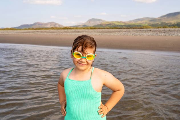 Smiling girl in swimming goggles looking at camera in shallow sea. Wales, England, United Kingdom CR_JNDO260222-1934983-01 ,model released, Symbolfoto