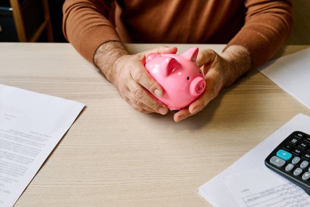 Man holding piggy bank at table with bills and calculator at home model released, Symbolfoto property released, CATF00870