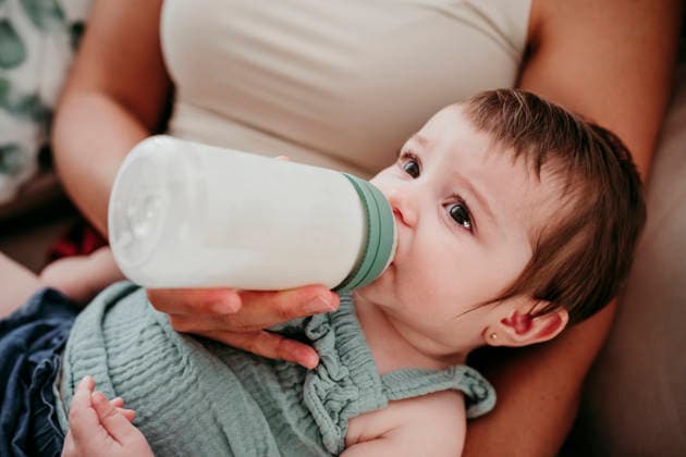 Mother bottle feeding baby on sofa at home enjoying quality time model released, Symbolfoto property released, EBBF09322
