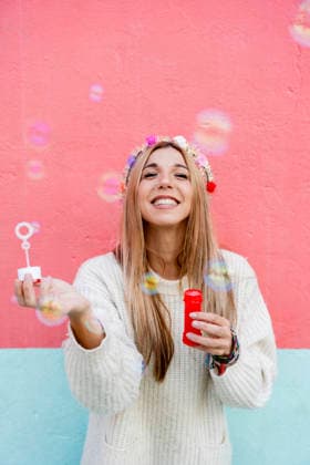 Smiling woman with flower crown blowing bubbles against pink wall model released, Symbolfoto, JMHMF01436