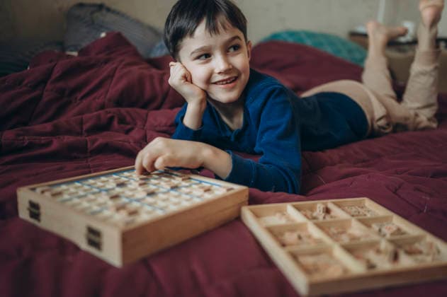 Child lying on bed playing Sudoku puzzle board game at home model released, Symbolfoto property released, ANAF05583
