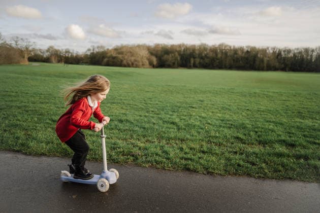 School girl in red cardigan riding scooter outdoors on lawn model released, Symbolfoto, IGEF00714