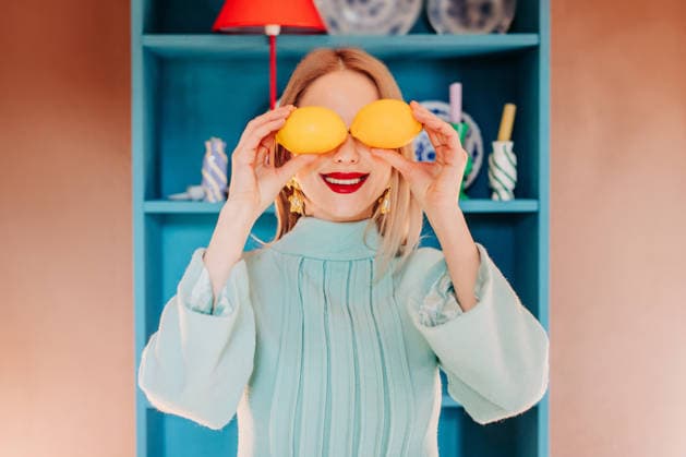 Smiling woman in blue dress holding lemons at eyes in colorful interior model released, Symbolfoto, VSNF04566