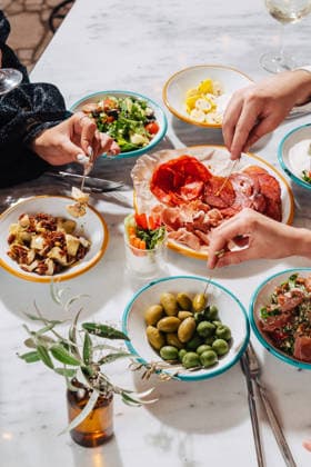 IMAGO Creative, Food, Tapas Unrecognizable hands enjoying a vibrant Mediterranean feast Cropped unrecognizable hands enjoy a Mediterranean meal with a variety of plates including olives, cured meats, salad, and artichokes on a white marble table. Model Released Andrerako_ID32184_1095647_002 Copyright: xAndrerakox RECORD DATE NOT STATED
